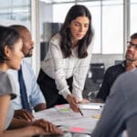 Architect working on blueprint with team to keep her money not just make it.