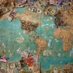 A map of the world with money showing you can travel on a budget if you think and talk money