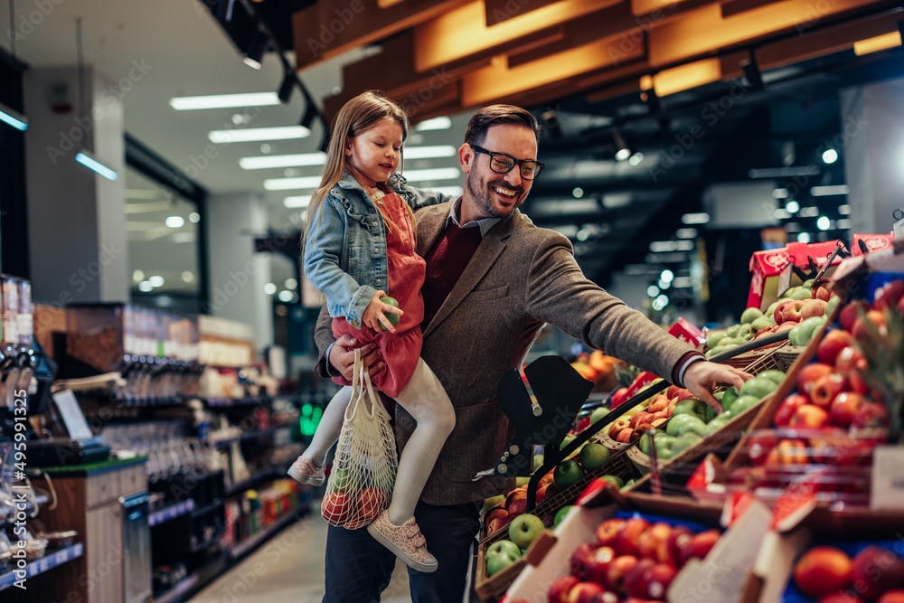 Father and daughter buying apples in grocery store as part of rising cost of living nationally