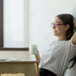 Satisfied young woman holding hand behind head and drinking coffee because she has any easy budgeting plan with Think and Talk Money.