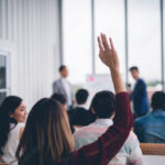 Woman raised up hands and arms to ask a question about money to the financial wellness professor
