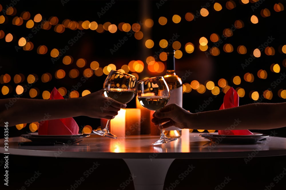 Young couple with glasses of wine having romantic candlelight dinner at table, closeup because they budgeted after learning about think and talk money.