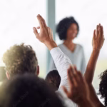 People raising hands in a meeting in response to a question illustrating that 8 out of 10 people have debt as learned on Think and Talk Money.