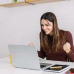 Excited young adult businesswoman feeling happy after receiving good news that she got a raise, which she learned how to use by tracking her savings rate on Think and Talk Money.