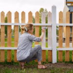 Woman sitting on haunches and painting fence representing the big financial decisions ahead of each of us and how talking about those decisions can only help us as learned on Think and Talk Money.