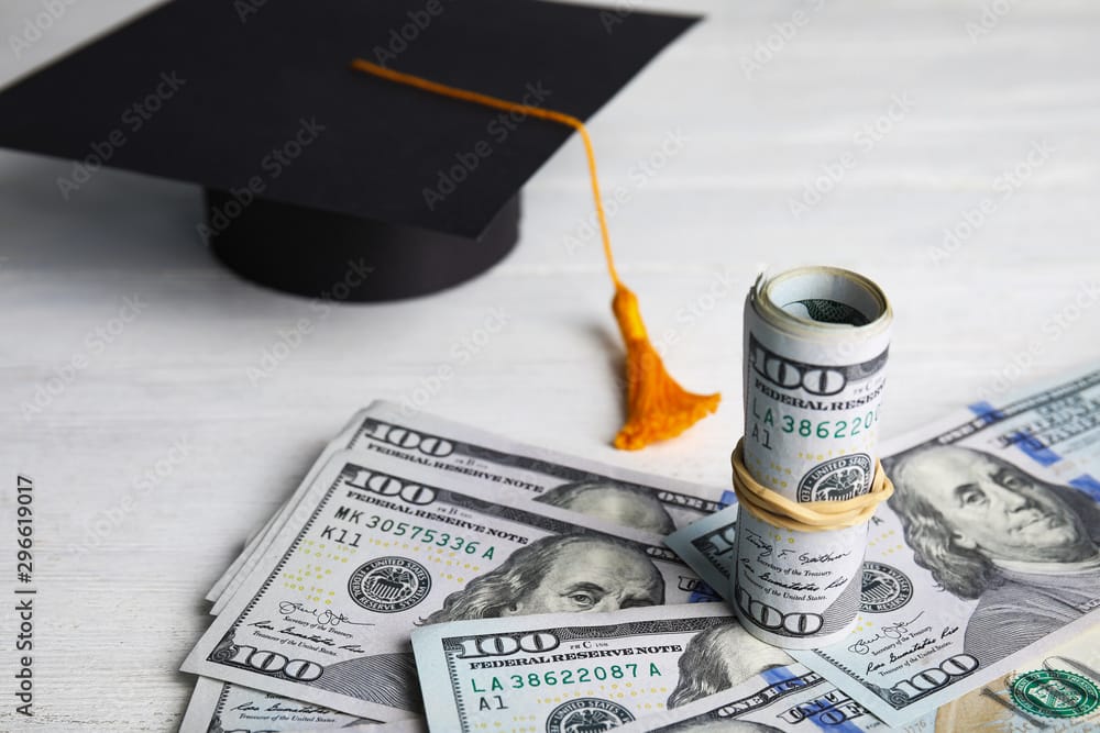 Dollar banknotes and student graduation hat on white wooden background illustrating Think and Talk Money's 10 student loan tips for lawyers and professionals.