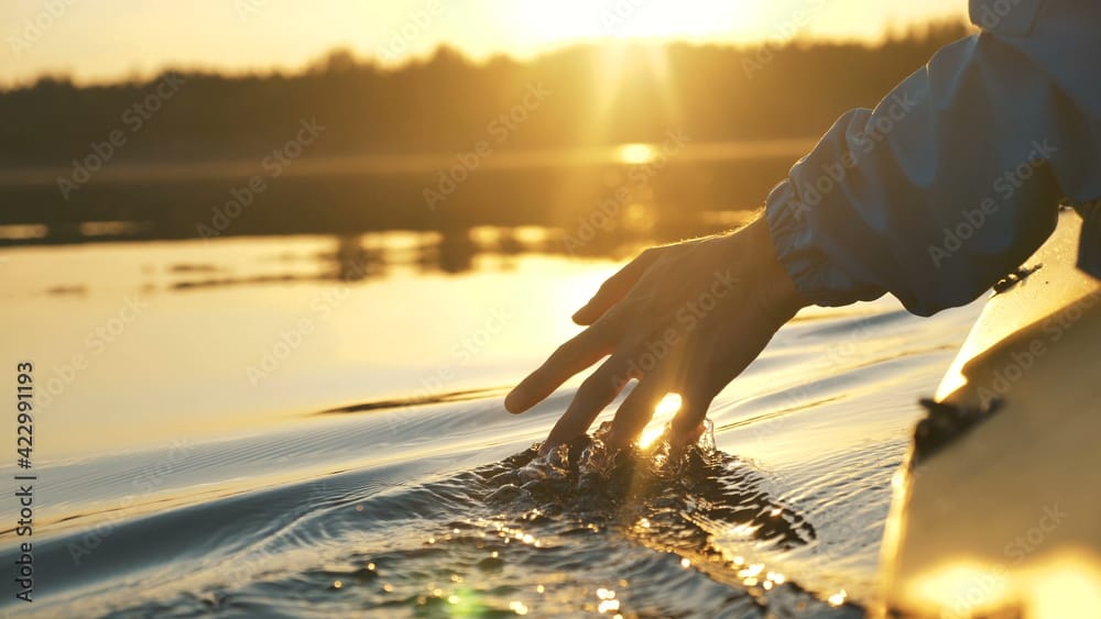man puts fingers down in lake kayaking against backdrop of golden sunset, unity harmony nature illustrating staying calm when markets are in free fall.