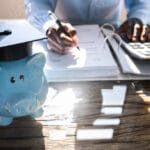 Picture of piggy bank on desk with person working on Student Loan options as learned on Think and Talk Money.