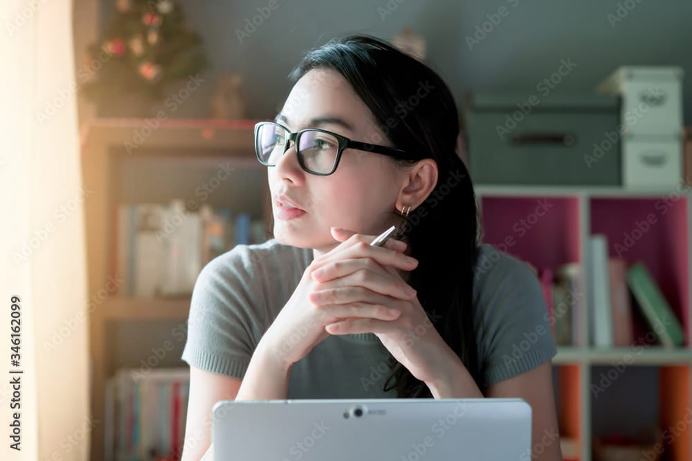 Woman thoughtful about work at home office desk laptop wondering whether she is saving too much for retirement.