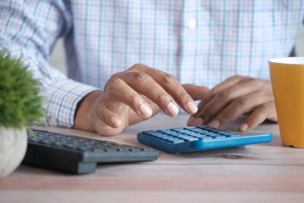 Close up of man hand using calculator to figure out whether to invest while in debt.