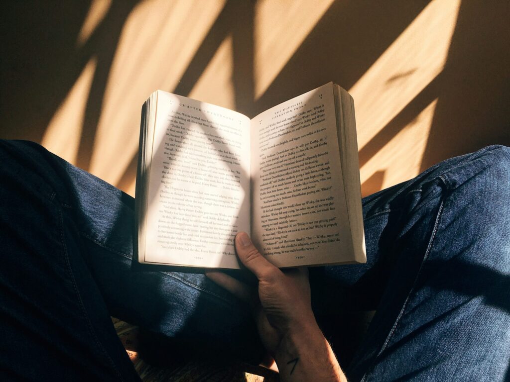 person holding book sitting on brown surface illustrating the need to read Millionaire Milestones by Sam Dogen