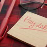 a note that says pay debt next to a pen and glasses indicating that other people pay my debt when I own real estate.