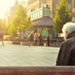 man sitting on brown wooden bench thinking about how he invested for retirement early on while also saving for college.