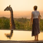 Photo taken at Mara Bushtops in Masai Mara, Kenya. Mara Bushtops conserves a large amount of land outside the national reserve which has resulted in wildlife population increases. This Giraffe, Called Harry comes right in to the resort and was very lucky to capture this special moment of a girl standing by the swimming pool saying hello to Harry the Giraffe, illustrating what I would do with $10 million.