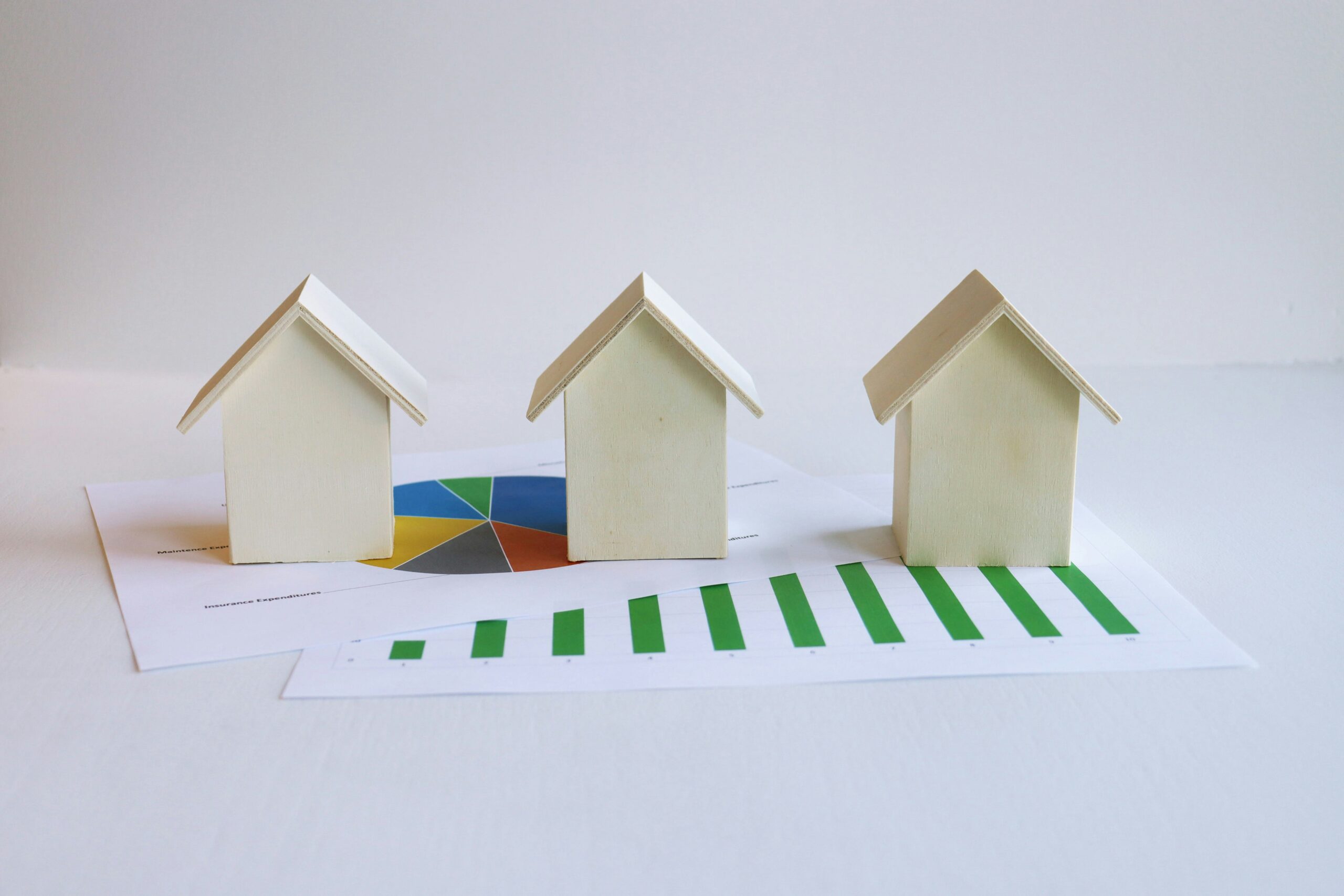 Three small houses sitting on top of a piece of paper illustrating how to generate long-term wealth through appreciation in real estate.