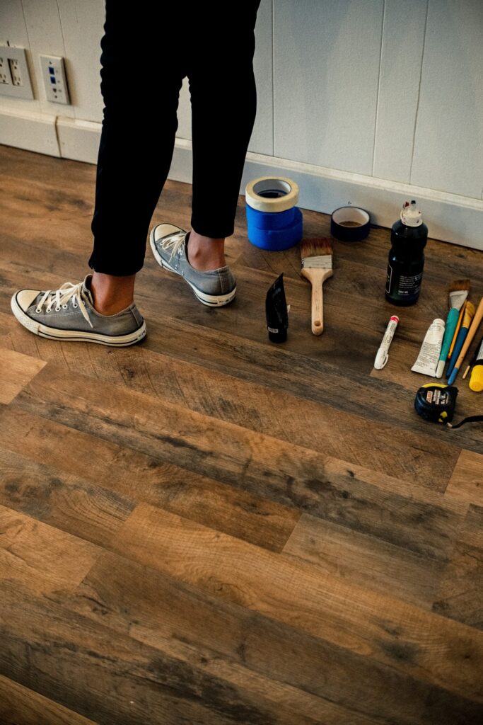 person in black pants and white and black sneakers standing on brown wooden floors about to do repairs as a landlord because owning rental properties is not passive income.