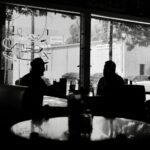 two people sitting at a table in front of a window thinking and talking about money.
