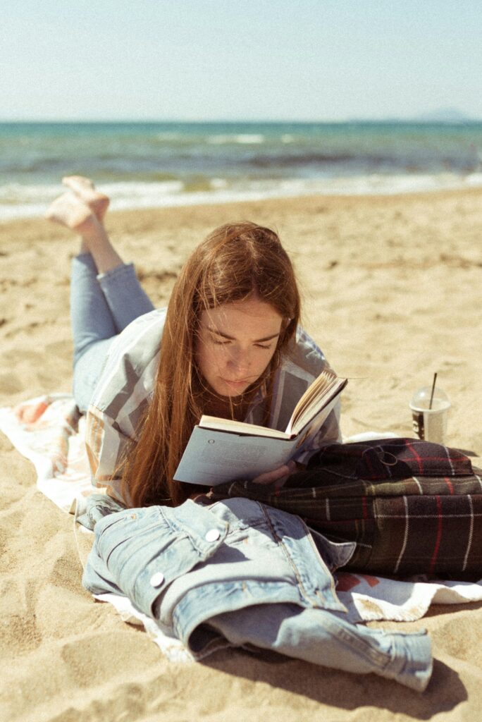 woman in white long sleeve shirt reading book on beach during daytime because she is financially free and bought her time back.