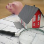 white and red wooden house beside grey framed magnifying glass to show you how to use CoCROI and ROI to evaluate different investments.