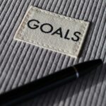 black and silver pen on gray notepad illustrating that now is the perfect time to revisit your money goals for the year.