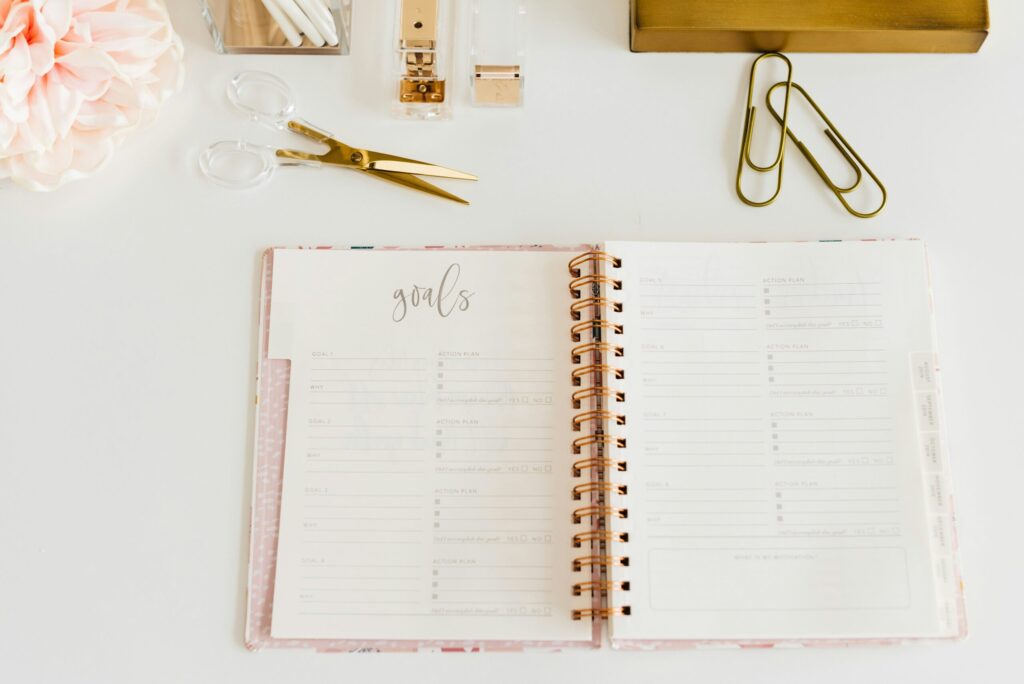scissors and two paper clips beside opened spiral notebook which is perfect for revisiting your 2025 money goals.