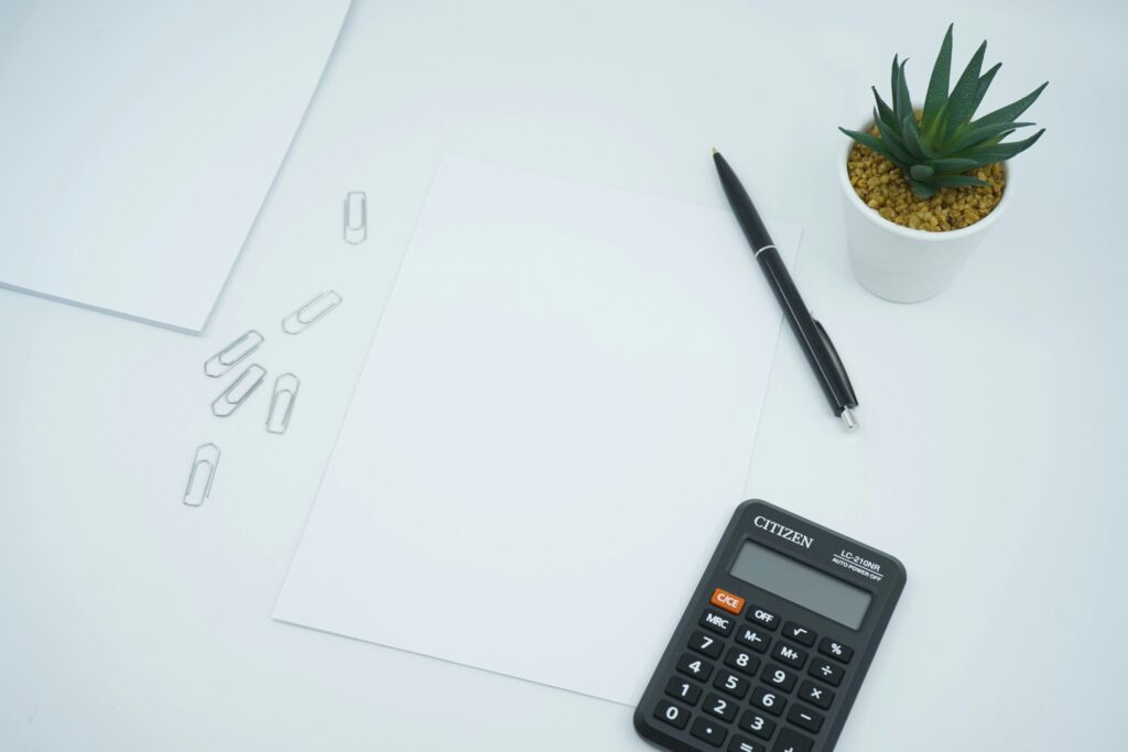 A financial and money themed photo featuring a blank paper on a desk next to a pen and calculator indicating how to make a budget to pay off debt.