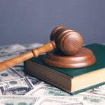 brown gavel and green book and money indicating that if you're a lawyer in debt, you make plenty of money and the problem is not your income.