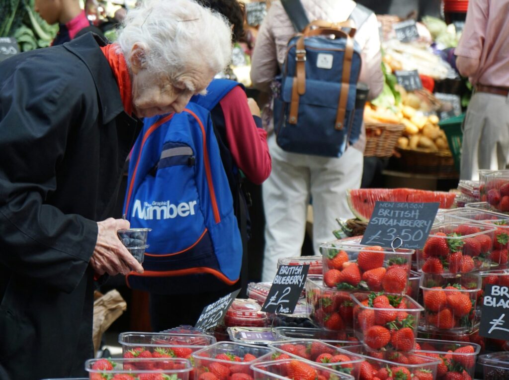 Old Caucasian woman shopping for fruit and choosing wisely like what a landlord needs to do when selecting tenants.