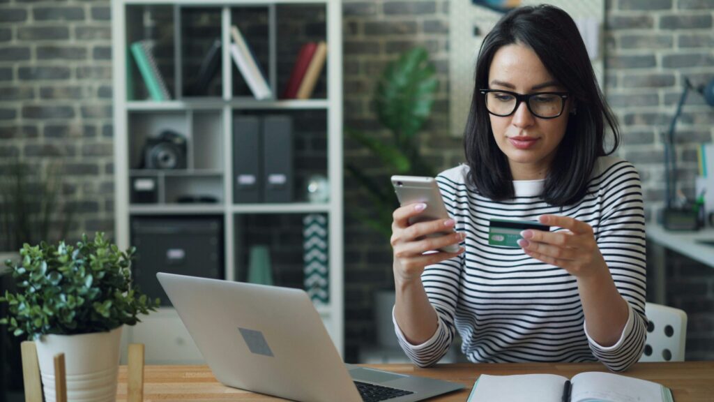 Portrait of young woman making payment with credit card using smartphone at work showing 10 tips to pay off debt for lawyers and professionals.