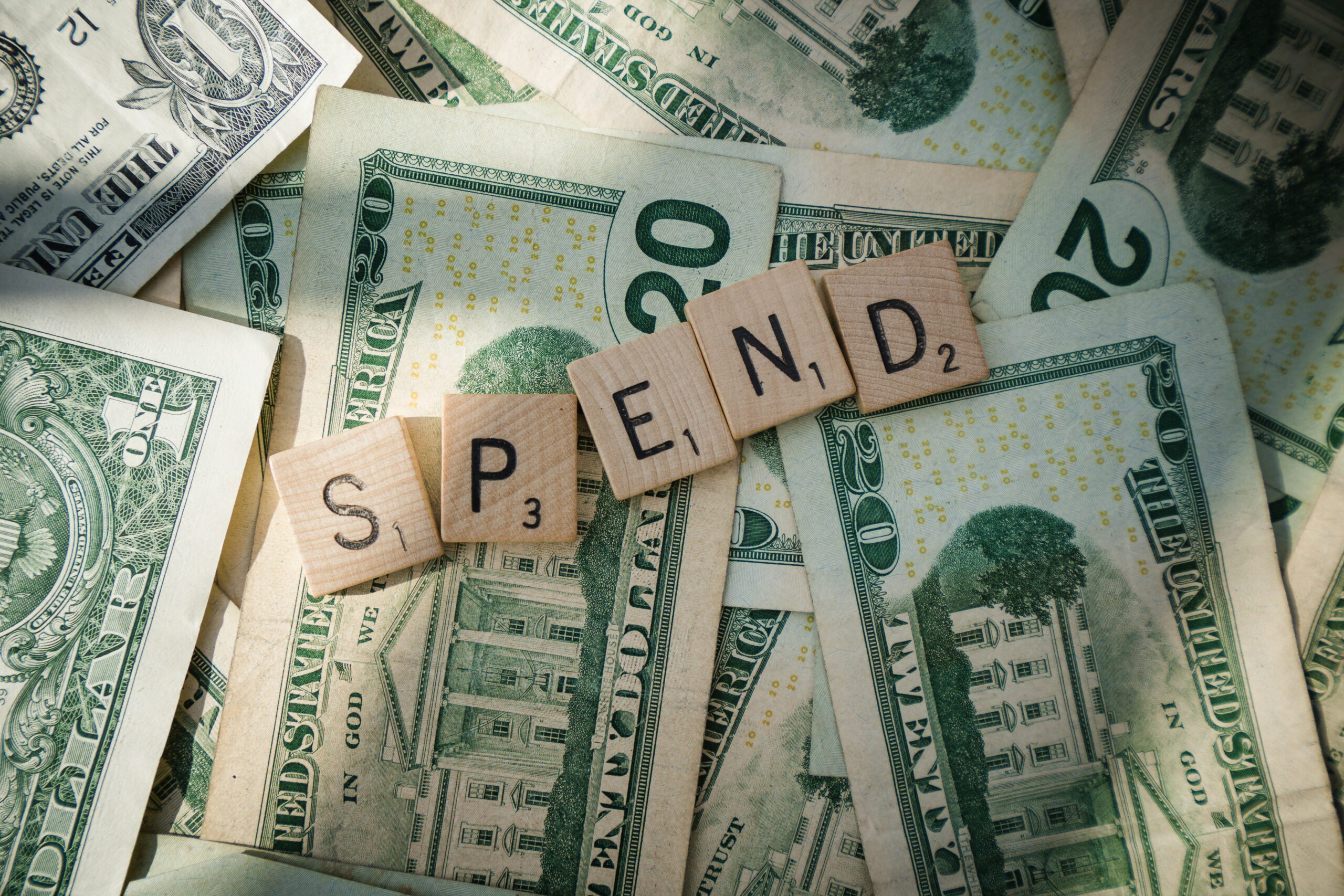 Scrabble letters spelling 'spend' on American bills showing how to make a budget to pay off debt.