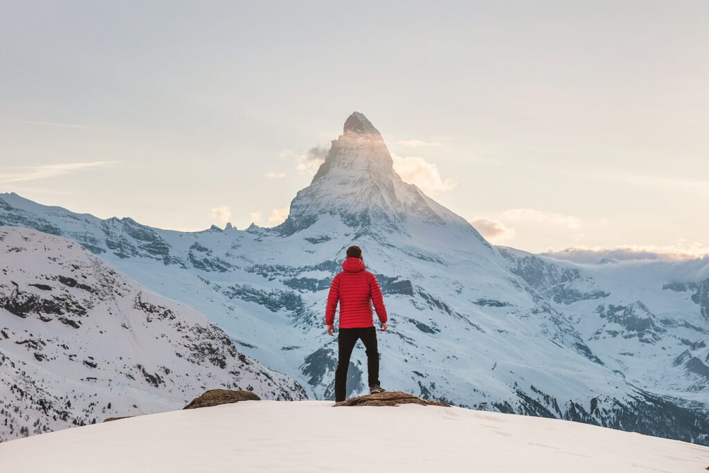 person in red hoodie standing on snowy mountain showing that ambitious goals do not make you a failure even if you don't hit them.