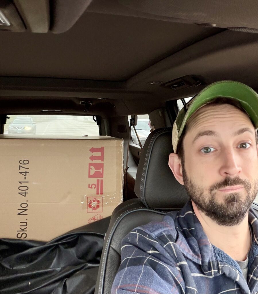 Matthew Adair picking up a big box from warehouse reflecting what he spends money on and doesn't like it or not like it but has to do it.