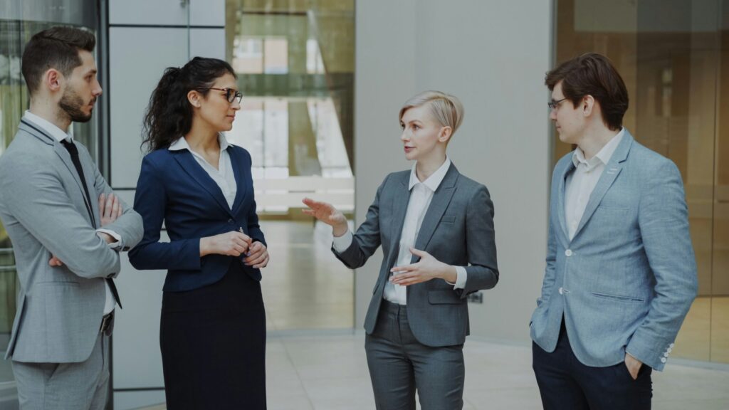 Businesswoman talking to her colleagues while standing in office lobby indoors about personal finance fundamentals for lawyers.