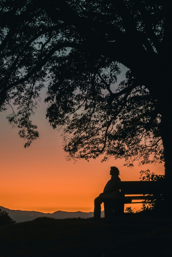 man sitting on bench during sunset showing that when markets decline it's important to chill and not make sudden investing mistakes.