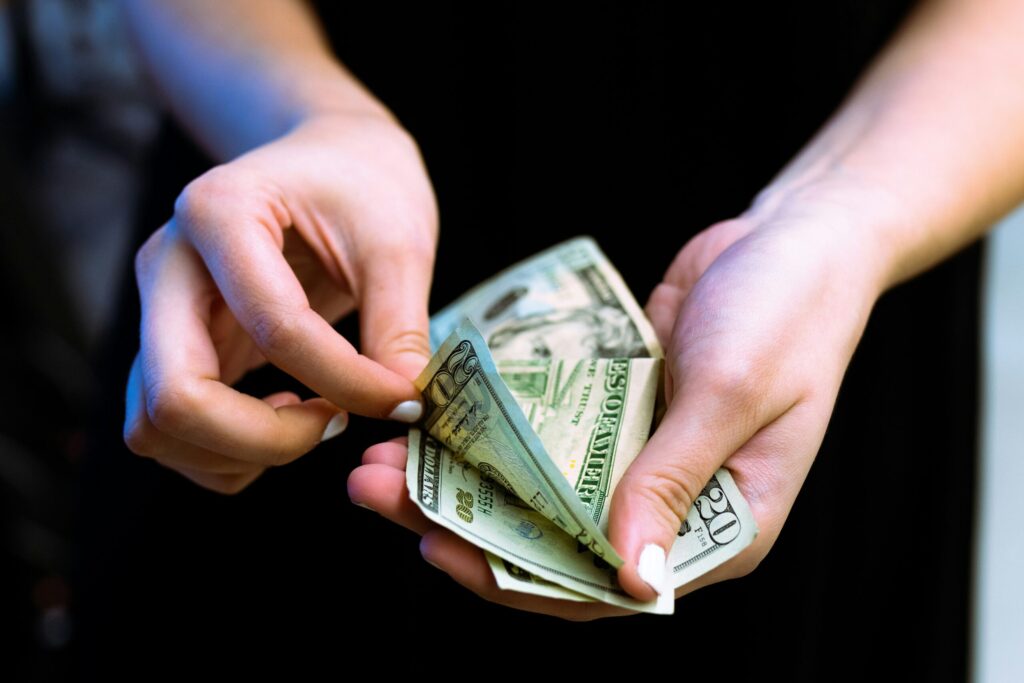 person holding fan of 100 US dollar bills indicating that figuring out why you want to be good with money is the first step to financial fulfillment.